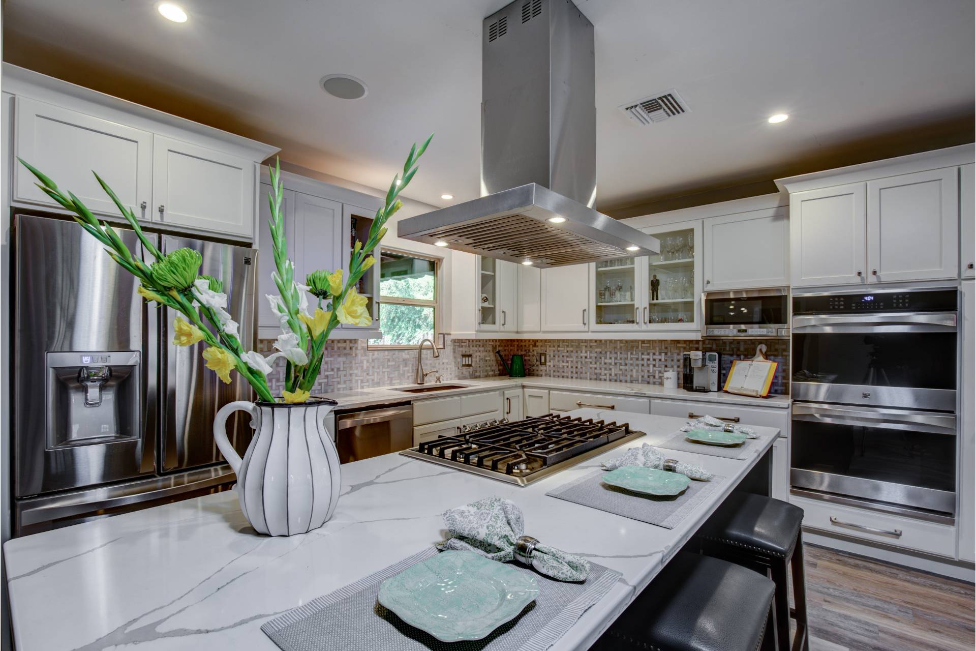 Distefano kitchen island with a white marble-look waterfall top, an integrated gas cooktop, a stainless island hood, and a basketweave tile backsplash