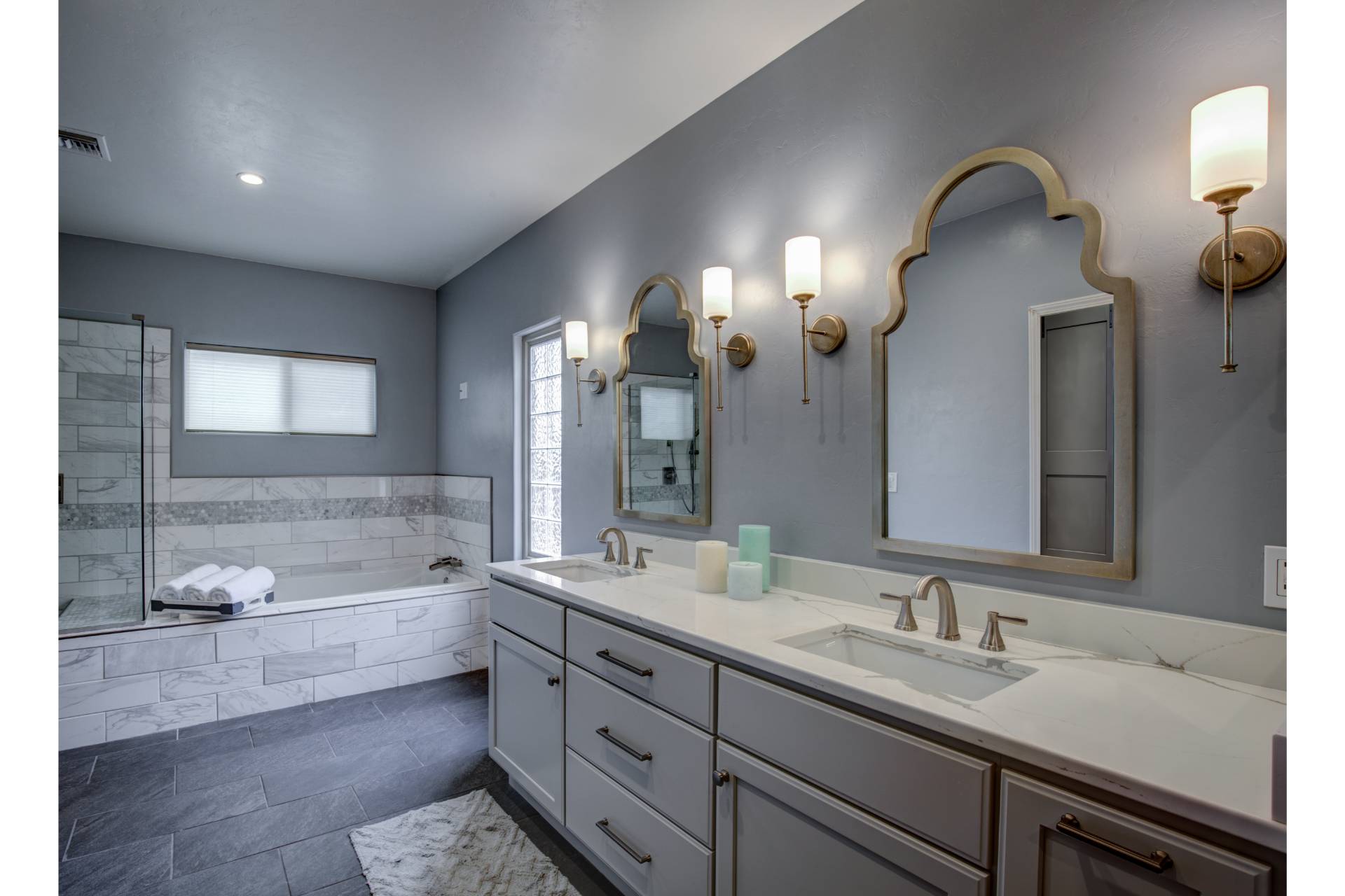 Distefano primary bath with a double vanity, quartz counters, arched gold-framed mirrors, and a marble-tiled soaking tub