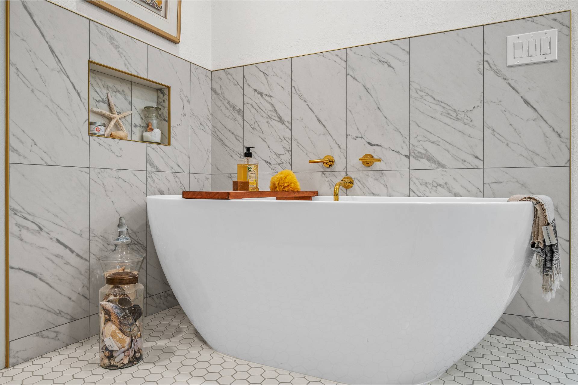 Gaudielle freestanding soaking tub against a marble-tile wall with polished-gold wall-mount filler and a hexagon mosaic floor