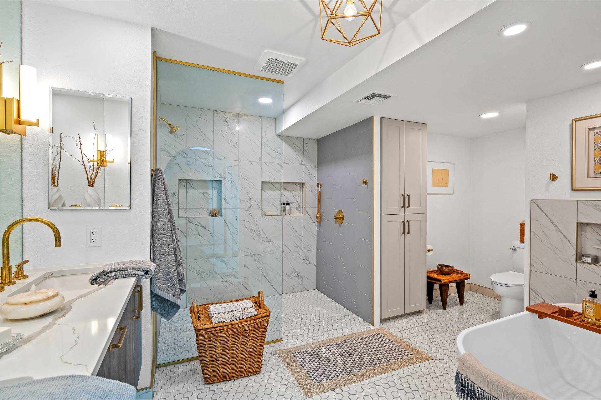 Gaudielle primary bath with a curbless marble-tile walk-in shower, hexagon accent wall, gold fixtures, and a hexagon mosaic floor under a geometric brass pendant