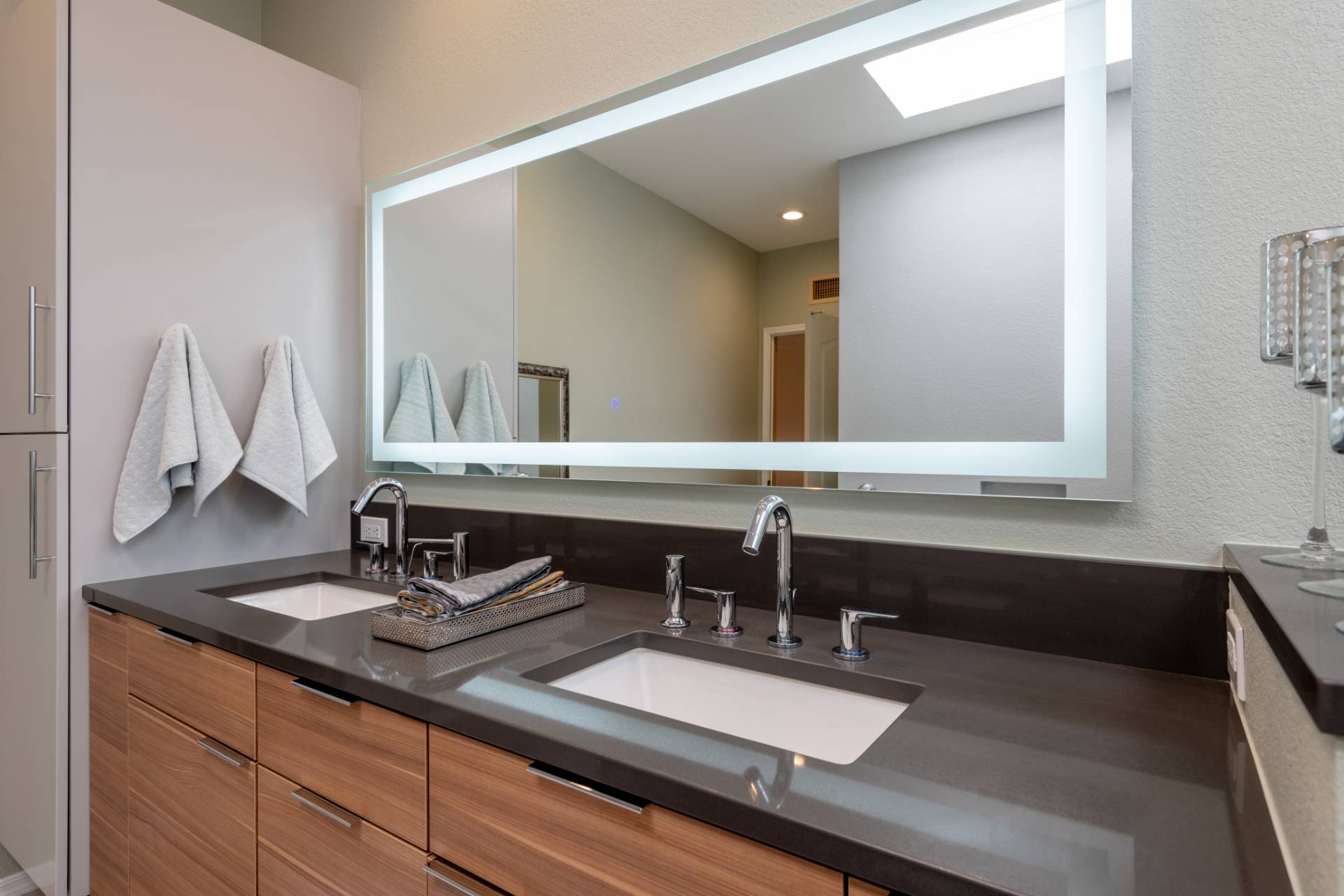 Close view of the Greenberg walnut double vanity with twin white undermount sinks, polished-chrome fixtures, and a large edge-lit LED mirror