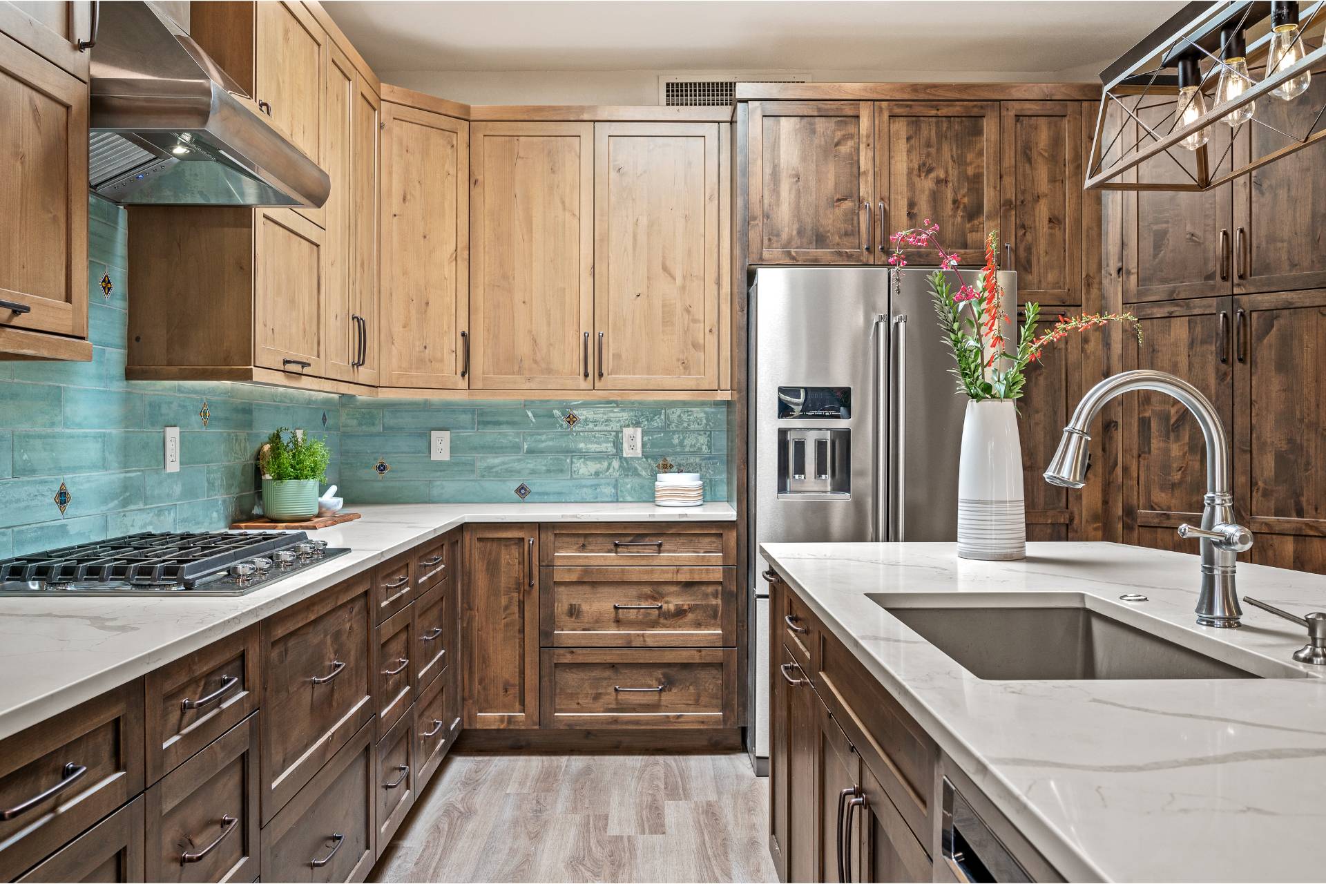 Hydukovich cooktop wall with a stainless under-cabinet hood, a black gas cooktop, and a glossy teal subway backsplash with painted accent tiles