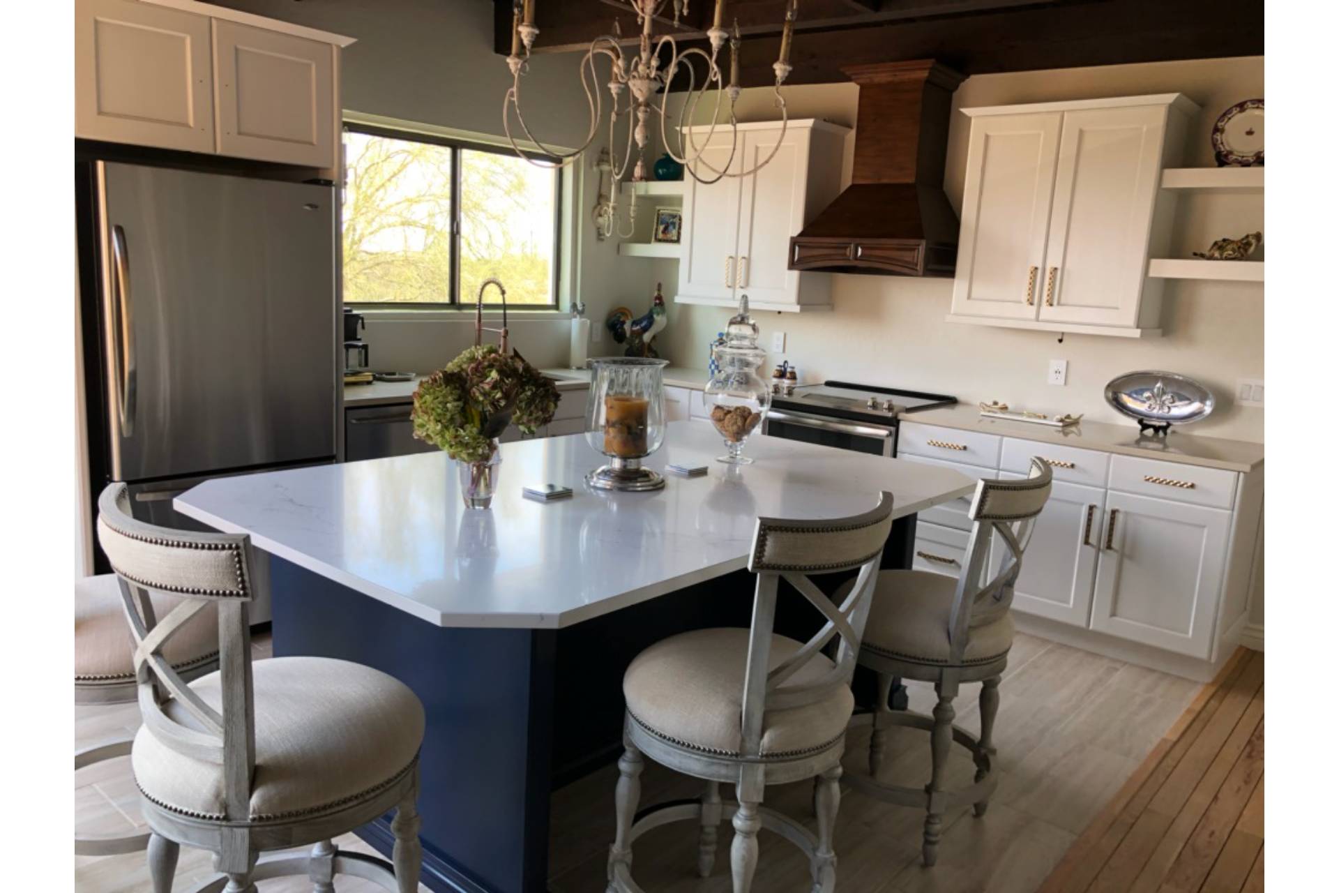 Keeley kitchen and dining island in white cabinetry with a navy-painted island, quartz waterfall top, and upholstered counter stools under a wrought-iron chandelier