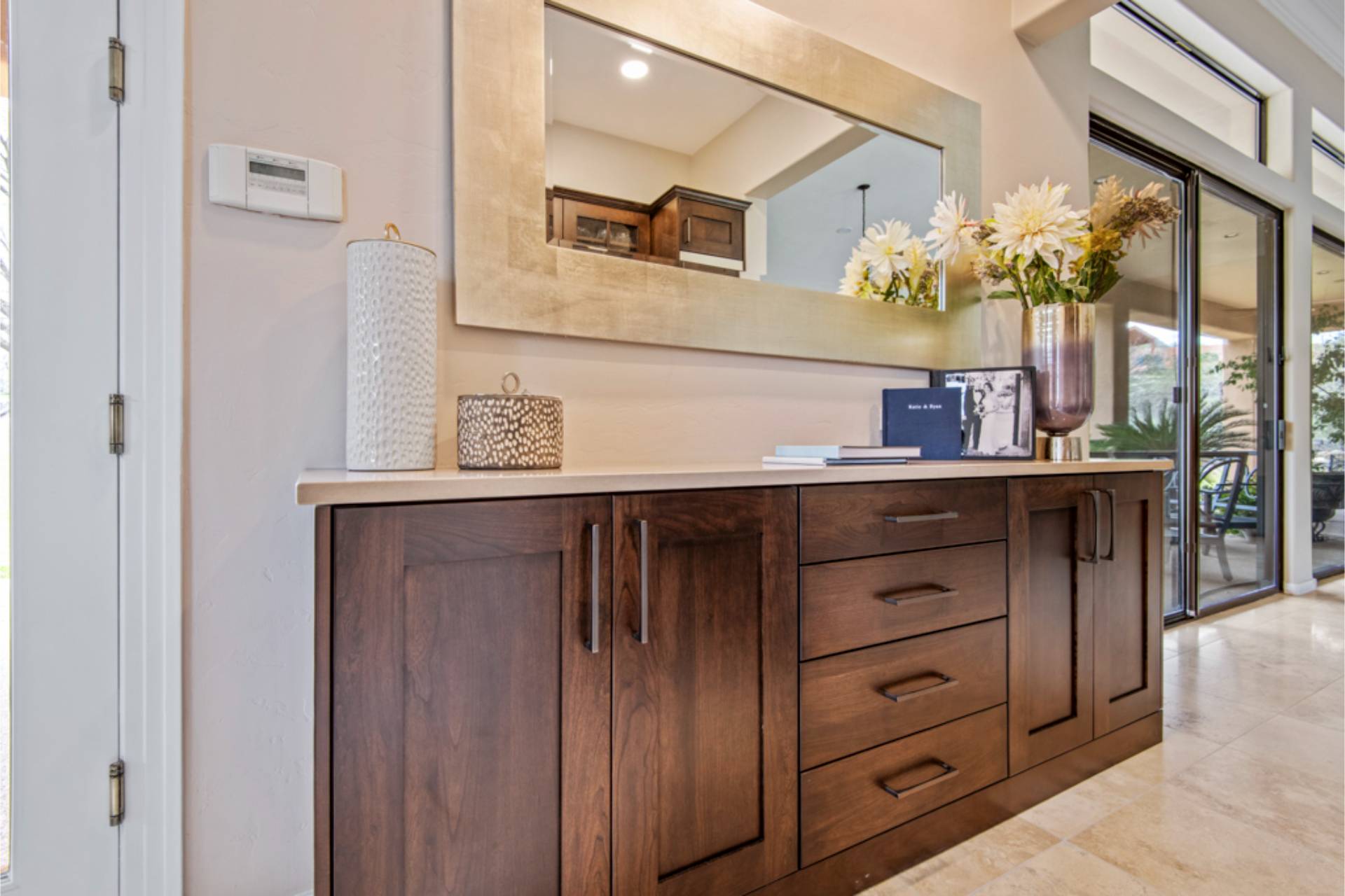 La Reserve bar and buffet cabinet in walnut with a stone top and a gold-framed mirror, opening to the patio