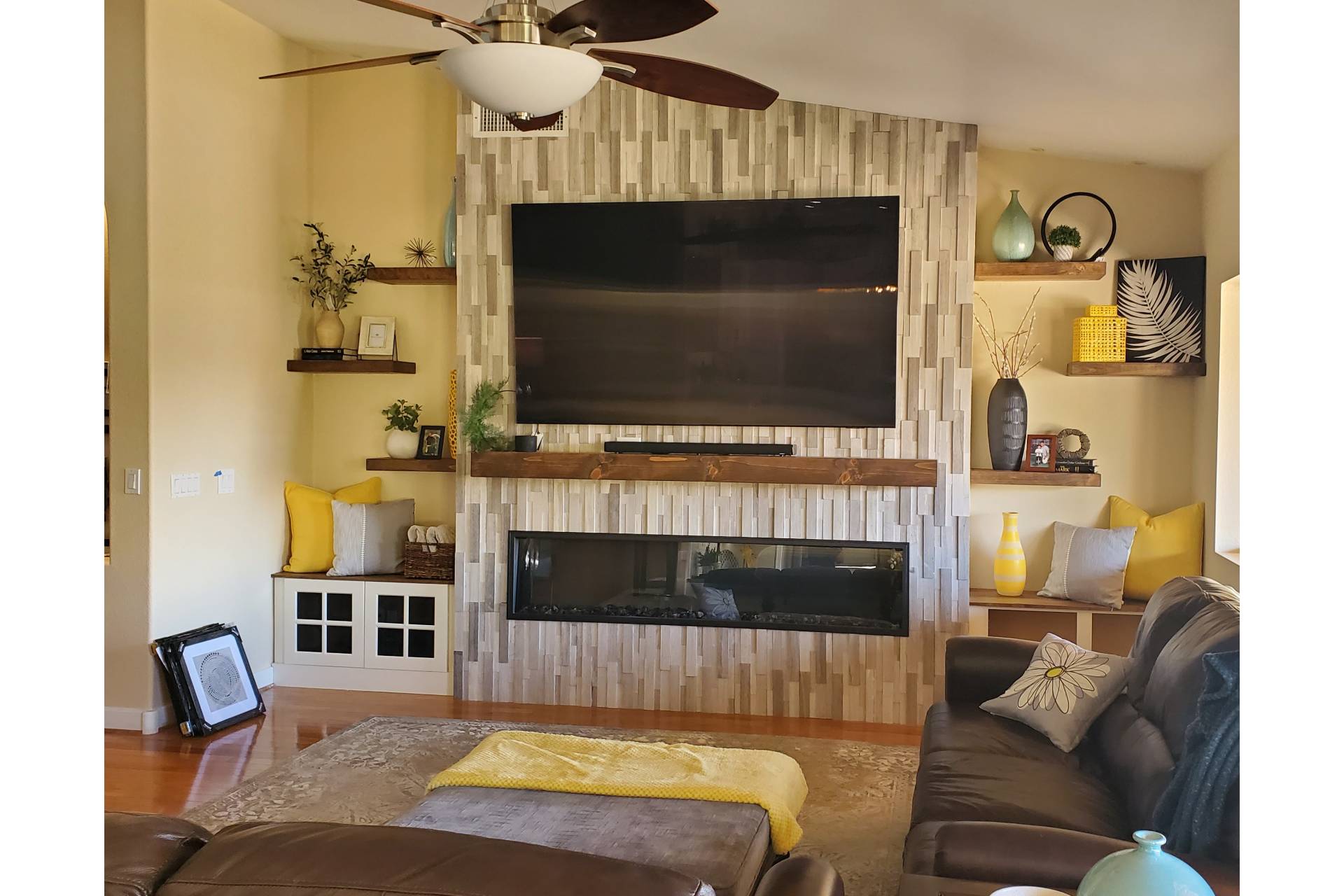 Nevenhoven great-room feature wall clad in stacked-wood tile with a mounted TV, linear gas fireplace, stained-wood mantel, and floating shelves