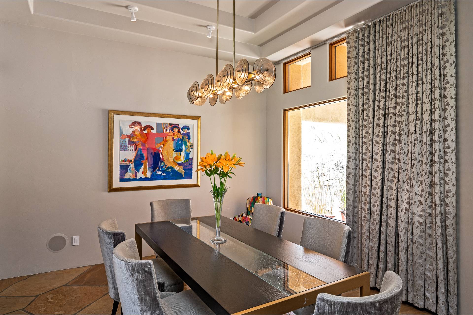 Ponder dining room with a glass-topped table, velvet chairs, a disc chandelier, and a bold framed artwork