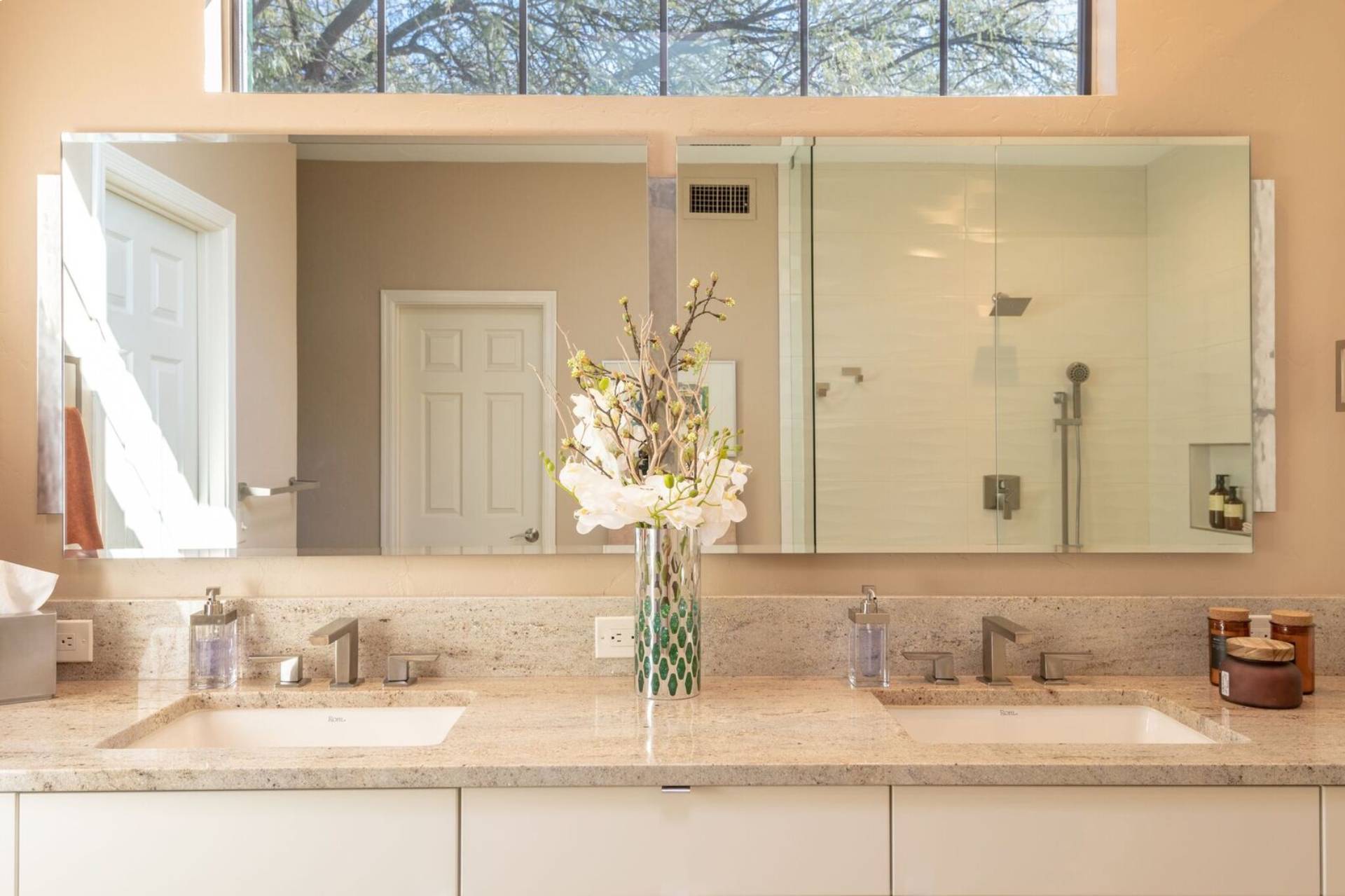 Schneider double vanity with a speckled granite top, twin undermount sinks, a full-width mirror, and a clerestory window framing a mesquite tree
